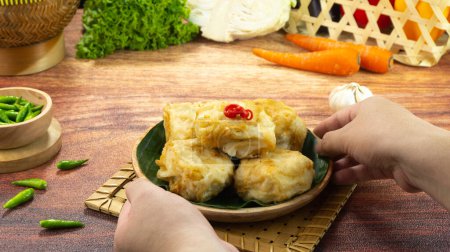 Photo for Deep fried Tofu or Tahu goreng is a traditional food from Indonesia made of tofu covered in flour batter with a mixture and spices served in a plate on dark wood background with hand. Close up - Royalty Free Image