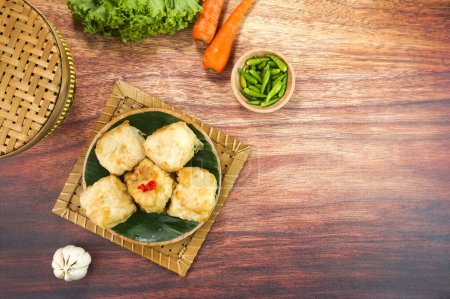 Photo for Deep fried Tofu or Tahu goreng is a traditional food from Indonesia made of tofu covered in flour batter with a mixture and spices served in a plate on dark wood background. Top view copy space - Royalty Free Image