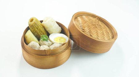 Téléchargez les photos : Boulettes de gâteau de poisson ou Siomay est un aliment traditionnel de l'Indonésie faite de pomme de terre oeuf chou rouleau cacahuète chili citron vert servi dans un bol en bambou isolé sur fond blanc vif. Gros plan - en image libre de droit