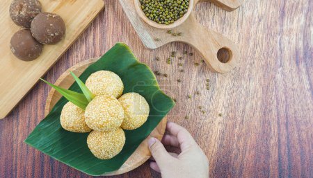 Téléchargez les photos : Boules de graines de sésame ou onde onde est un aliment traditionnel de l'Indonésie faite de farine de riz gluant haricots verts graines de sésame sucre brun servi dans une assiette sur fond de bois avec la main - en image libre de droit