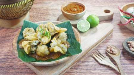 Téléchargez les photos : Le bakso frit et le tofu ou Batagor est un aliment traditionnel indonésien composé de boulettes d'assaisonnement de tapioca de poisson sauce épicée aux arachides servie dans une assiette sur fond de bois sombre. Gros plan - en image libre de droit
