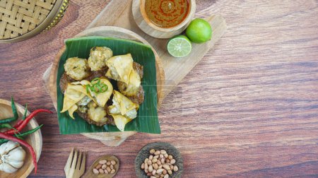Téléchargez les photos : Le bakso frit et le tofu ou Batagor est un aliment traditionnel indonésien à base de boulettes d'assaisonnement de tapioca de poisson sauce épicée aux arachides servie dans une assiette sur fond de bois sombre. - en image libre de droit