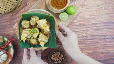 Téléchargez les photos : Le bakso frit et le tofu ou Batagor est un aliment traditionnel indonésien à base de boulettes d'assaisonnement de tapioca de poisson sauce épicée aux arachides servie dans une assiette sur fond de bois sombre avec espace de copie vue du dessus - en image libre de droit