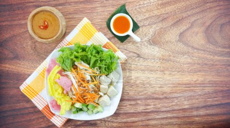 Téléchargez les photos : La salade de légumes crus ou Asinan Betawi est un aliment traditionnel indonésien composé de craquelins de sauce aux arachides au tofu à la laitue au chou et servi dans une assiette sur fond de bois sombre. Espace de copie de vue supérieure - en image libre de droit