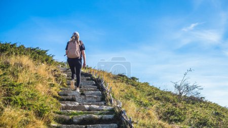 Photo for Girl climbing to the top by stone steps with green grass. Landscape with a young woman with a backpack. Travel and tourism. Hiking. Climbing - Royalty Free Image