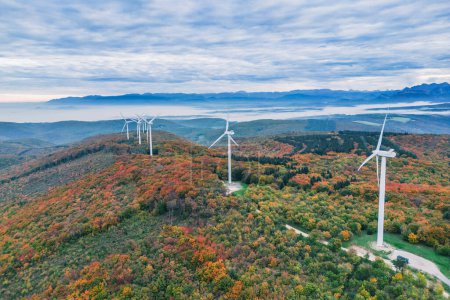 Photo for Turbine windmills for energy production. Renewable energy sources. Windmills situated on a hill overgrown with trees. Overlooking the surrounding mountains during autumn - Royalty Free Image