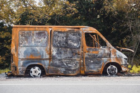 Photo for Burnt out big van next to the road. The car after the accident. A burnt-out car without windows and tires - Royalty Free Image