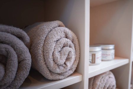 Luxuriöse und elegante Badezimmerhandtücher ordentlich in einem Regal angeordnet, mit einer Vielzahl von Größen und Formen. Die Gesamtatmosphäre ist entspannend und beruhigend, perfekt für ein Wellness-Erlebnis.