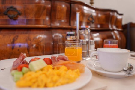 Foto de Una vista de ángulo lateral de una mesa de desayuno con un plato de fruta y una taza de café, con iluminación suave y difusa creando un ambiente cálido y cómodo. - Imagen libre de derechos