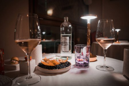 Photo for A romantic and elegant table setting with wine glasses and food in a dimly lit room, creating a relaxing atmosphere. Perfect for Venice, Italy-themed collections. - Royalty Free Image