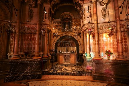 Photo for In a Barcelona chapel, an arch encircles the altar and a sacred icon, set against gold, red, and cream designs. The walls, pillars, and marble boast detailed patterns, while lamps cast a gentle light. - Royalty Free Image