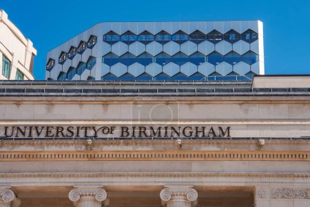 Una clásica fachada de la Universidad de Birmingham con UNIVERSIDAD DE BIRMINGHAM inscrita, contrasta un edificio moderno con un diseño de panal de miel y ventanas azules en Birmingham, Reino Unido.