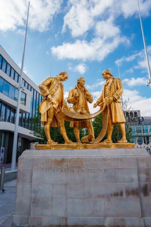 Téléchargez les photos : Statue dorée de Matthew Boulton, James Watt et William Murdoch à Birmingham, au Royaume-Uni, contre un bâtiment moderne et un ciel bleu, symbolisant le patrimoine industriel des villes. - en image libre de droit