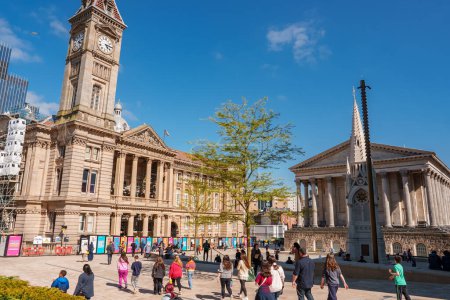Téléchargez les photos : Une place animée à Birmingham, au Royaume-Uni, avec des habitants profitant d'un temps ensoleillé, encadrée par des bâtiments historiques, y compris une tour d'horloge et un mémorial de guerre, faisant allusion au mélange de villes du passé et du présent. - en image libre de droit