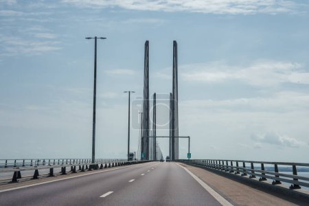 A modern, multilane Oresund Bridge under a clear sky connects Copenhagen, Denmark, with Malmo, Sweden, featuring tall pylons and a sleek cablesupported design.