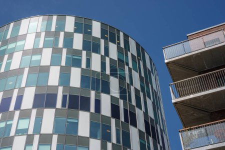 Téléchargez les photos : L'architecture moderne brille dans cette image, avec un bâtiment en verre cylindrique à côté d'une structure en béton avec des balcons, sous un ciel bleu clair, probablement à Copenhague. - en image libre de droit