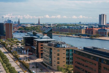Photo for Daytime cityscape from an elevated view, featuring modern midrise buildings with brick and glass facades, a treelined street, and a reflective water body with boats in Copenhagen, Denmark. - Royalty Free Image