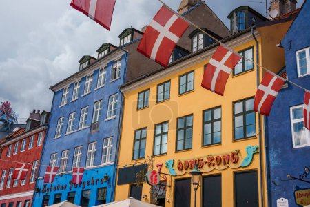 Photo for Vibrant Copenhagen street scene with colorful European buildings in blue, yellow, and red, Danish flags waving, and signs for a Hong Kong shop and a cafe. - Royalty Free Image