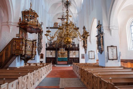Photo for Bright, airy church in Copenhagen or Malmo with white walls, arched ceilings, and a central aisle to a blue altar. Boasts a grand chandelier, carved wooden pulpit, and orderly pew rows. - Royalty Free Image