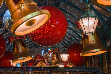 Téléchargez les photos : Des décorations d'intérieur Covent Garden avec des boules rouges surdimensionnées et des cloches dorées pendent du plafond voûté d'un marché traditionnel de Londres, créant une atmosphère chaleureuse et festive de Noël. - en image libre de droit
