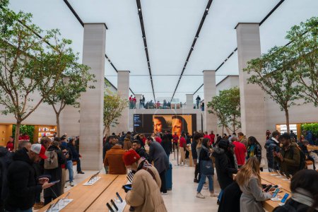 Téléchargez les photos : À l'intérieur d'un Apple Store londonien animé, la lumière naturelle illumine un design minimaliste avec de hauts plafonds, de longues tables présentant des produits technologiques et des clients engagés avec le personnel. - en image libre de droit