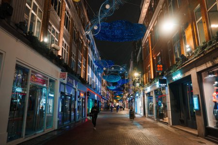 Photo for An enchanting evening view of a London street during Christmas, with vibrant blue lights and decorations creating a cozy canopy above bustling shoppers and classic architecture. - Royalty Free Image