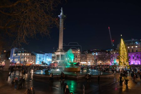Foto de Una velada festiva en Trafalgar Square, Londres, con la Columna Nelsons brillando, un árbol de Navidad noruego iluminando la escena, y edificios históricos adornados con luces coloridas. - Imagen libre de derechos