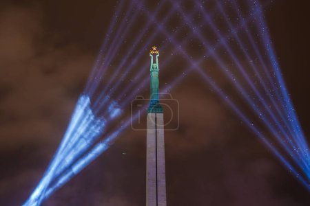 Téléchargez les photos : Illuminated Freedom Monument à Riga, Lettonie, brille de lumières bleues la nuit, symbolisant l'indépendance des nations. Une femme aux trois étoiles couronne le monument, représentant les régions lettones. - en image libre de droit
