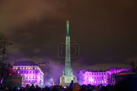 Photo for Illuminated Freedom Monument in Riga stands tall during Latvias Independence Day celebrations, surrounded by a festive crowd and bathed in purple hues and spotlights. - Royalty Free Image