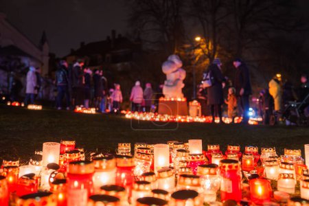 Foto de Vigilia vespertina en Letonia con velas encendidas para el Día de la Independencia, proyectando un cálido resplandor sobre la hierba mientras la gente se reúne en un parque, reflejándose en un homenaje común y solemne.. - Imagen libre de derechos