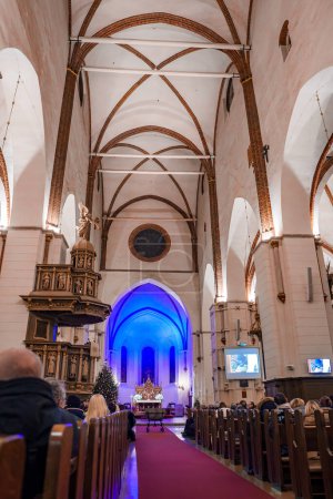 Foto de Interior de la catedral de Riga Dome durante un servicio con congregantes en bancos oscuros, altar bluelit con retablos dorados, árbol de Navidad y pantallas modernas, probablemente en Letonia para el Día de la Independencia. - Imagen libre de derechos