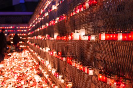 Téléchargez les photos : Une exposition solennelle de bougies avec des porte-bougies rouges, probablement pour le Jour de l'indépendance de la Lettonie, émet une lueur chaude le long d'un mur renforcé, créant une ambiance respectueuse. - en image libre de droit