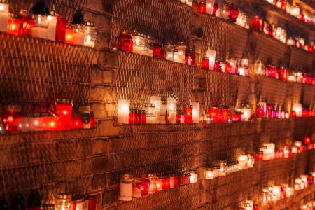 Téléchargez les photos : Un ensemble de bougies rouges et blanches dans des porte-verre placés dans un treillis métallique, émettant une lueur tranquille, probablement partie du souvenir de la fête de l'indépendance de la Lettonie. - en image libre de droit