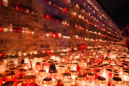 Téléchargez les photos : Des rangées de bougies dans des bocaux en verre coloré illuminent un événement solennel en Lettonie, projetant une lueur chaude pour honorer la fête de l'indépendance, avec les lumières s'étendant au loin. - en image libre de droit
