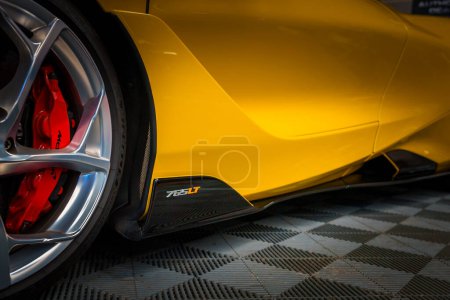 Téléchargez les photos : Gros plan d'un profil latéral élégant McLaren 765LT jaune près de la roue arrière, soulignant sa conception aérodynamique, son étrier de frein rouge et sa roue en alliage d'argent sur un plancher à carreaux. - en image libre de droit