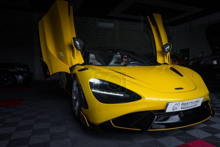 Téléchargez les photos : Une McLaren 765LT jaune vif, dont les portes dièdres s'ouvrent, se trouve dans un garage d'accordage sur un plancher à carreaux. La lumière dramatique souligne sa forme élégante et son front audacieux avec un logo remarquable. - en image libre de droit