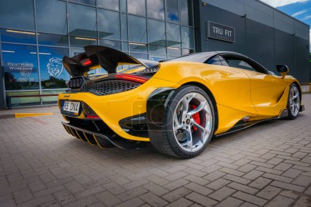 Téléchargez les photos : Un McLaren 765LT jaune vif avec un aileron surélevé et des évents hexagonaux est garé à l'extérieur d'un bâtiment, mettant en valeur son design aérodynamique et son profil sportif.. - en image libre de droit
