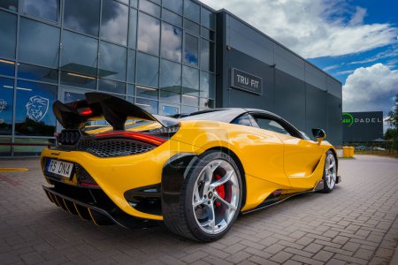 Photo for A vibrant yellow McLaren 765LT with a raised rear wing and RS DNA license plate is parked outside a modern building with TRU FIT and PADEL signage, showcasing its aerodynamic design and sporty look. - Royalty Free Image