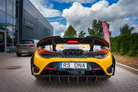 Photo for A vibrant yellow McLaren 765LT with an open rear engine cover, showcasing its mechanics, is parked outside the TRU FIT building in Latvia, featuring sleek aerodynamics and custom RS DNA plates. - Royalty Free Image