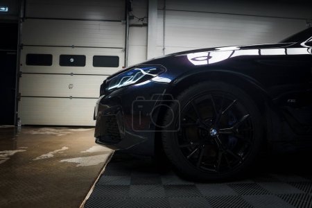 Photo for Closeup of a sleek BMW in a garage, showcasing its shiny black paint, angular LED headlights, and sporty multispoke wheels with performance tires and brakes. - Royalty Free Image