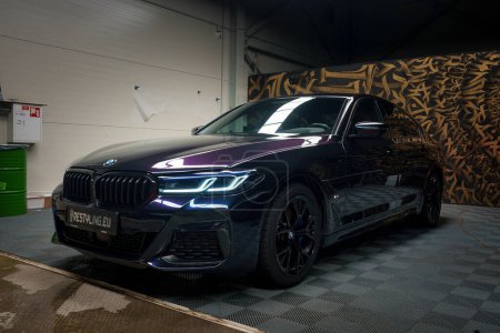 Photo for A sleek black BMW with illuminated LED headlights and kidney grille is parked in a garage, reflecting ambient light off its polished exterior and black rims, against a graffitistyle wall. - Royalty Free Image