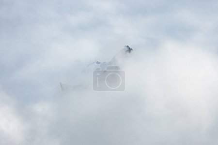 Photo for Misty mountain peaks emerge through clouds at Engelberg, with glimpses of a ski lift system, highlighting the serene Swiss Alps winter landscape and skiing ambiance. - Royalty Free Image