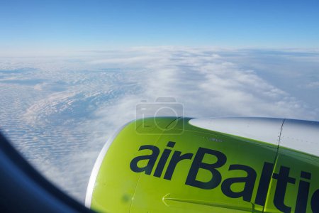 Leuchtend lindgrüne airBaltic Motorhauben ziehen in diesem Luftbild die Aufmerksamkeit auf sich, spiegeln den blauen Himmel wider und blicken auf ein Wolkenmeer. Ideal für Reisende, die Ruhe in der Höhe suchen.