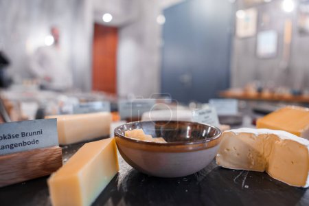 Téléchargez les photos : Gros plan de fromages assortis, coupés en différentes formes pour la dégustation, avec un bol de condiment au centre, sur fond d'intérieur moderne à la station de ski Engelberg. - en image libre de droit