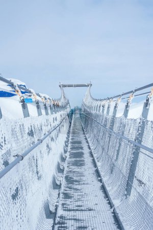 Téléchargez les photos : Scène hivernale d'un pont suspendu enneigé avec treillis métallique et mains courantes en corde à Engelberg, en Suisse, offrant une vue sur le terrain alpin sous un ciel couvert. - en image libre de droit