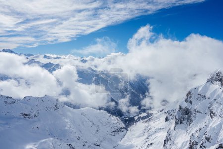 Breathtaking winter landscape of Engelberg, Switzerland, with snowcovered mountains under a bright blue sky dotted with fluffy clouds, perfect for skiing and snowboarding.
