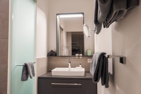 Luxury Engelberg resort bathroom with white sink, sleek cabinet, mirror light, plush towels, toiletries, and warm glow for an elegant atmosphere.