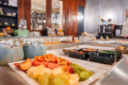 Téléchargez les photos : Gros plan d'un petit déjeuner buffet à Engelberg avec une assiette d'ananas, kiwi, pamplemousse et melon, entouré de condiments et bols, dans un cadre de restauration luxueux. - en image libre de droit