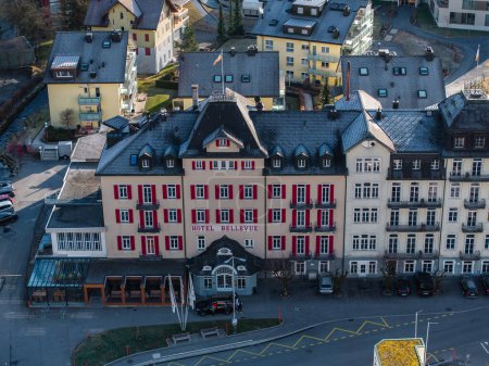 Photo for Aerial view of the grand Hotel Bellevue with a red facade in Engelberg, featuring a European alpine design, whitetrimmed windows, and a semicircular canopy entrance. - Royalty Free Image