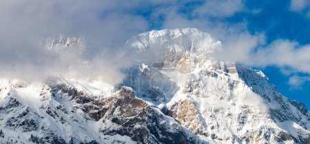 Die sonnenbeschienenen, schneebedeckten Gipfel von Engelberg, Schweiz, schaffen ein beeindruckendes Spiel von Licht und Schatten, mit klarem blauem Himmel und wehenden Wolken, die die alpine Pracht verstärken.